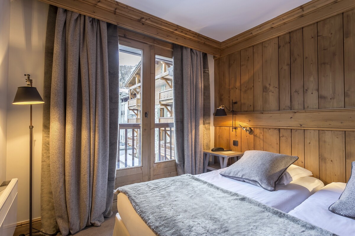 Ein Schlafzimmer mit Bett, Lampe, einer Holzwand und Blick auf ein Gebäude.