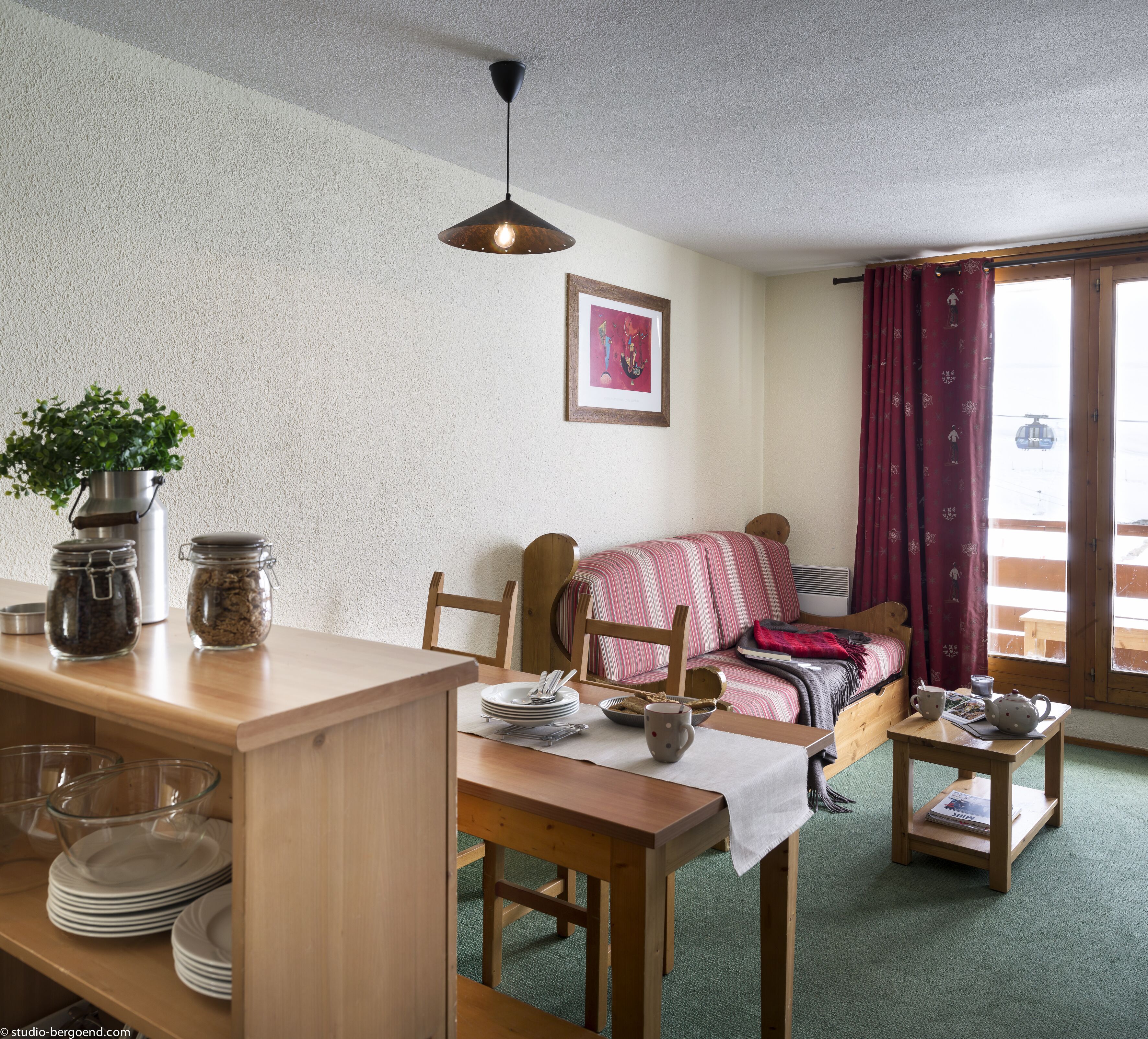 Ein gemütliches Zimmer mit einem Holzesstisch, einer Couch mit gestreifter Decke und einem Fenster mit Vorhängen.