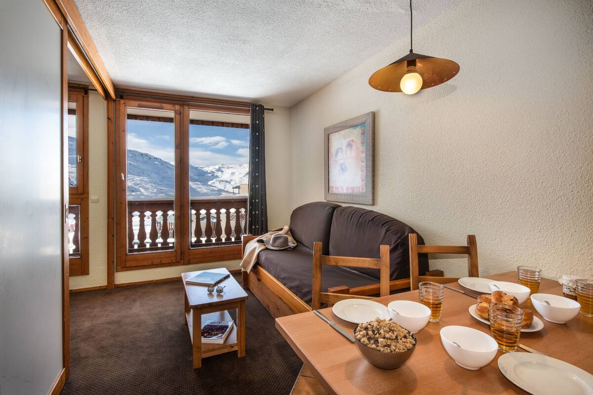 Una habitación acogedora con sofá, mesa de comedor y vistas a montañas a través de amplios ventanales.