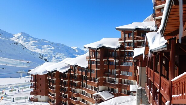 A multi-story hotel with balconies, a ski slope in the background, and a mountain range. - Residence le Cheval Blanc (Les Belleville)