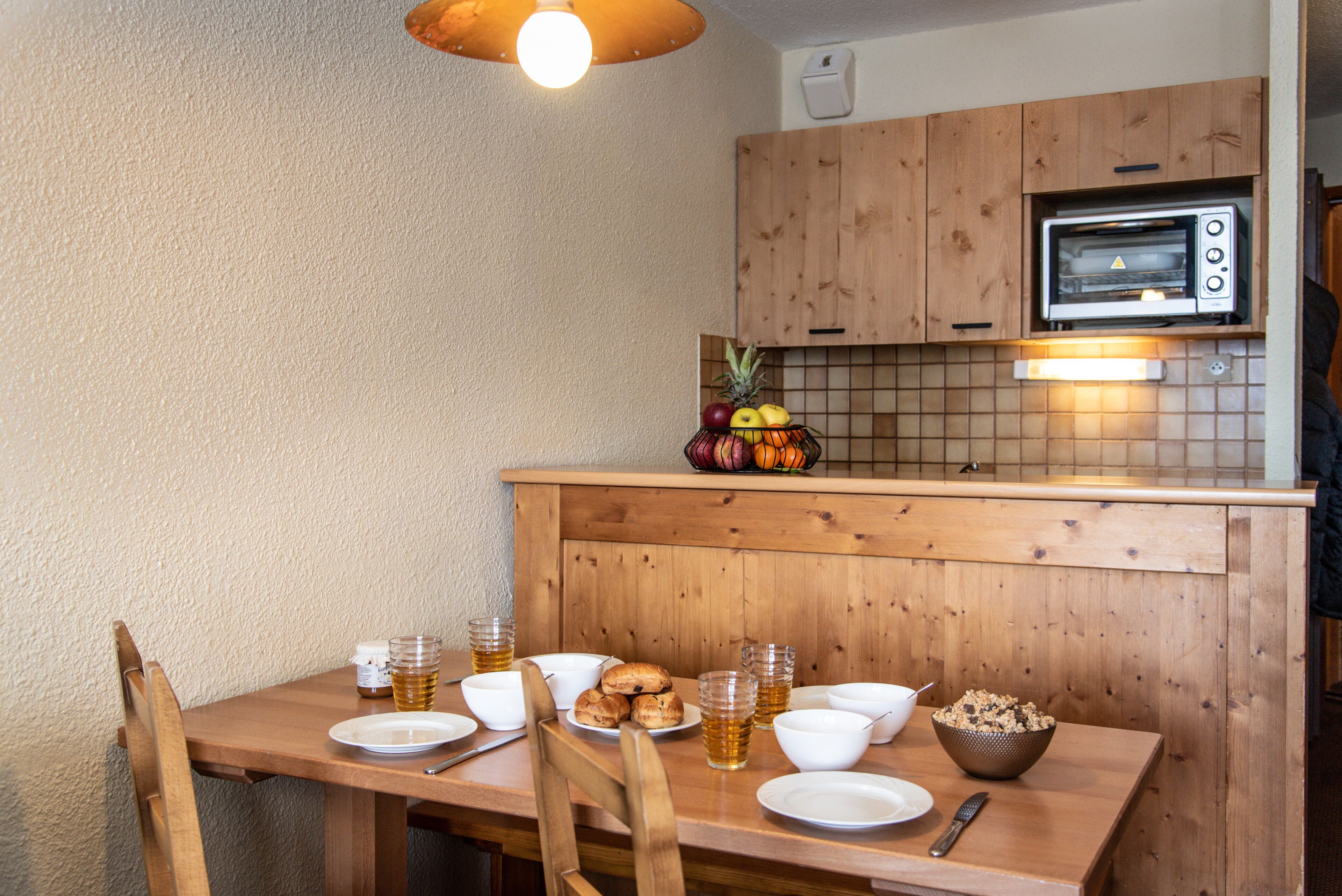 Una mesa de comedor de madera con platos, tazones y vasos de cerveza. Un microondas está sobre el mostrador.