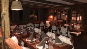 A dimly lit restaurant with wooden tables and chairs, each with a white furry throw. - Residence le Cheval Blanc (Les Belleville)