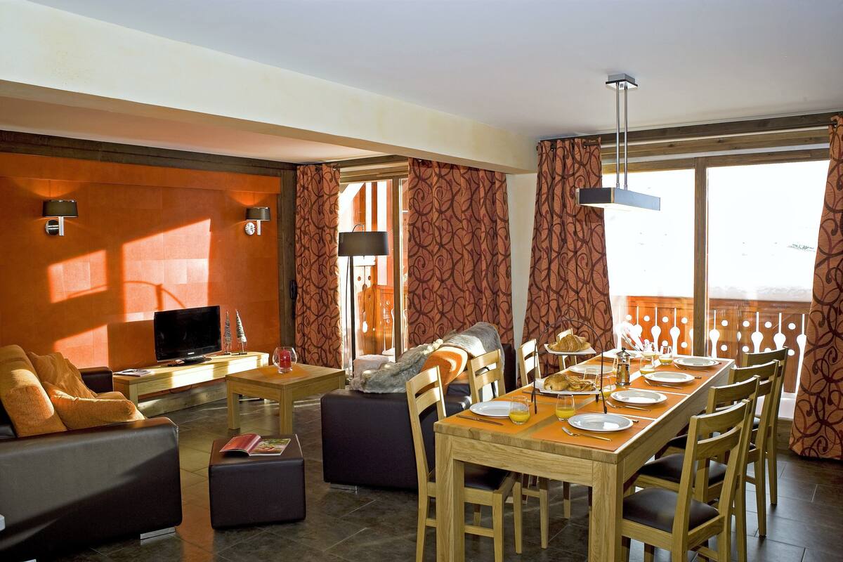 Un salon moderne avec un canapé, un téléviseur et un coin repas avec une table mise pour deux personnes.