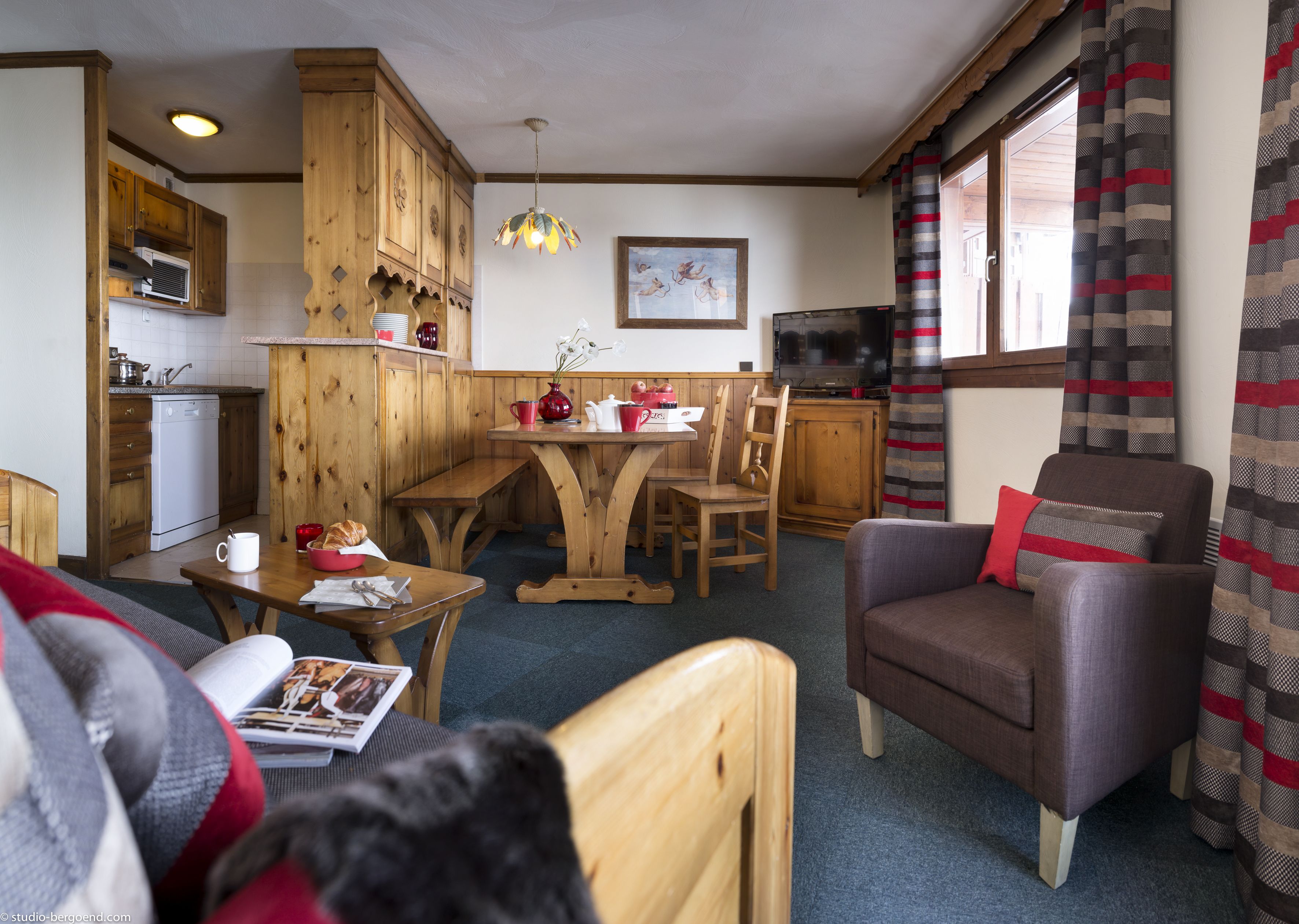 Un interior de cabaña acogedor con muebles de madera, una mesa de comedor, un televisor y una ventana con cortinas.
