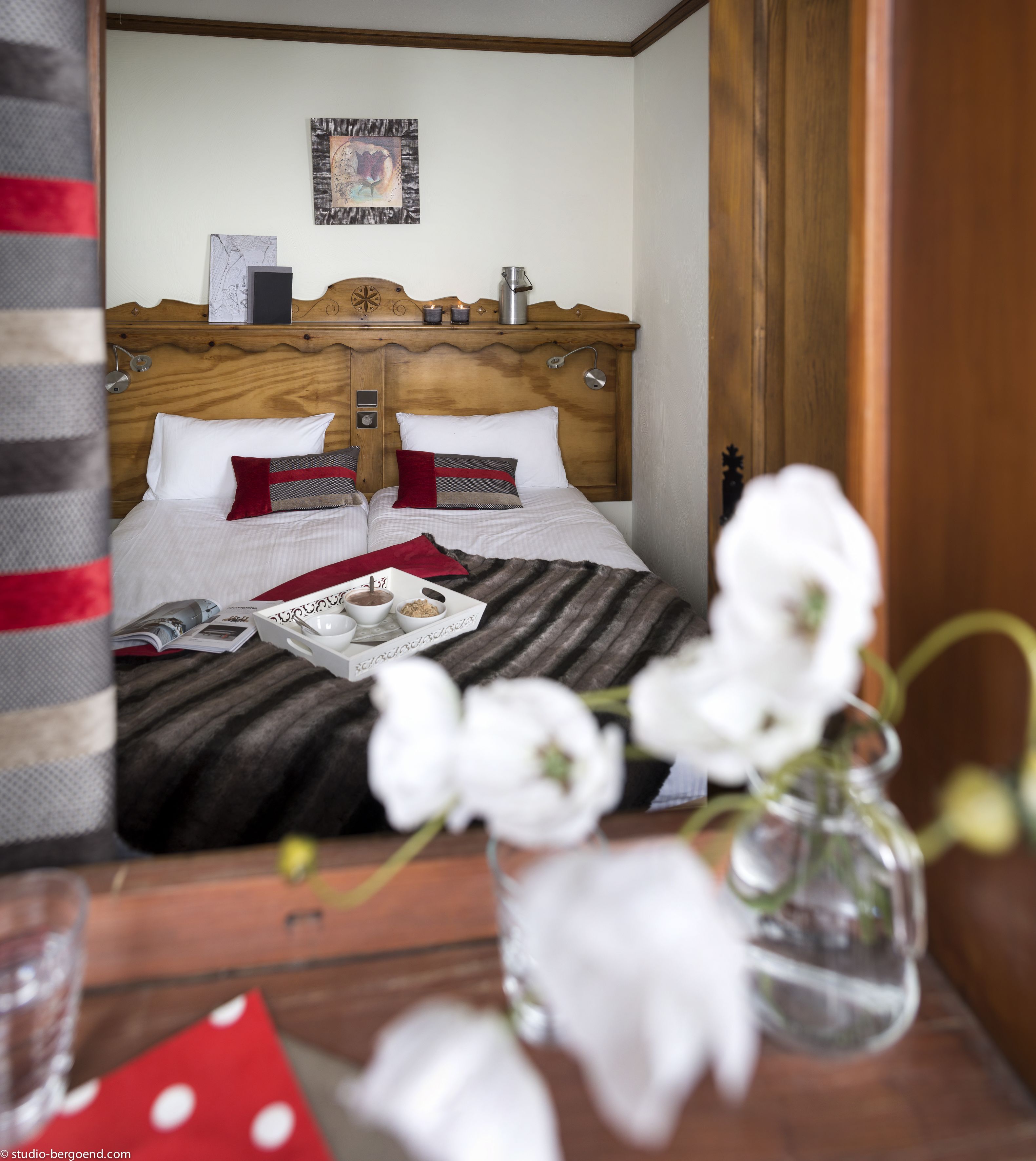 A neatly made bed with white and red pillows, a wooden headboard, and a framed picture above.