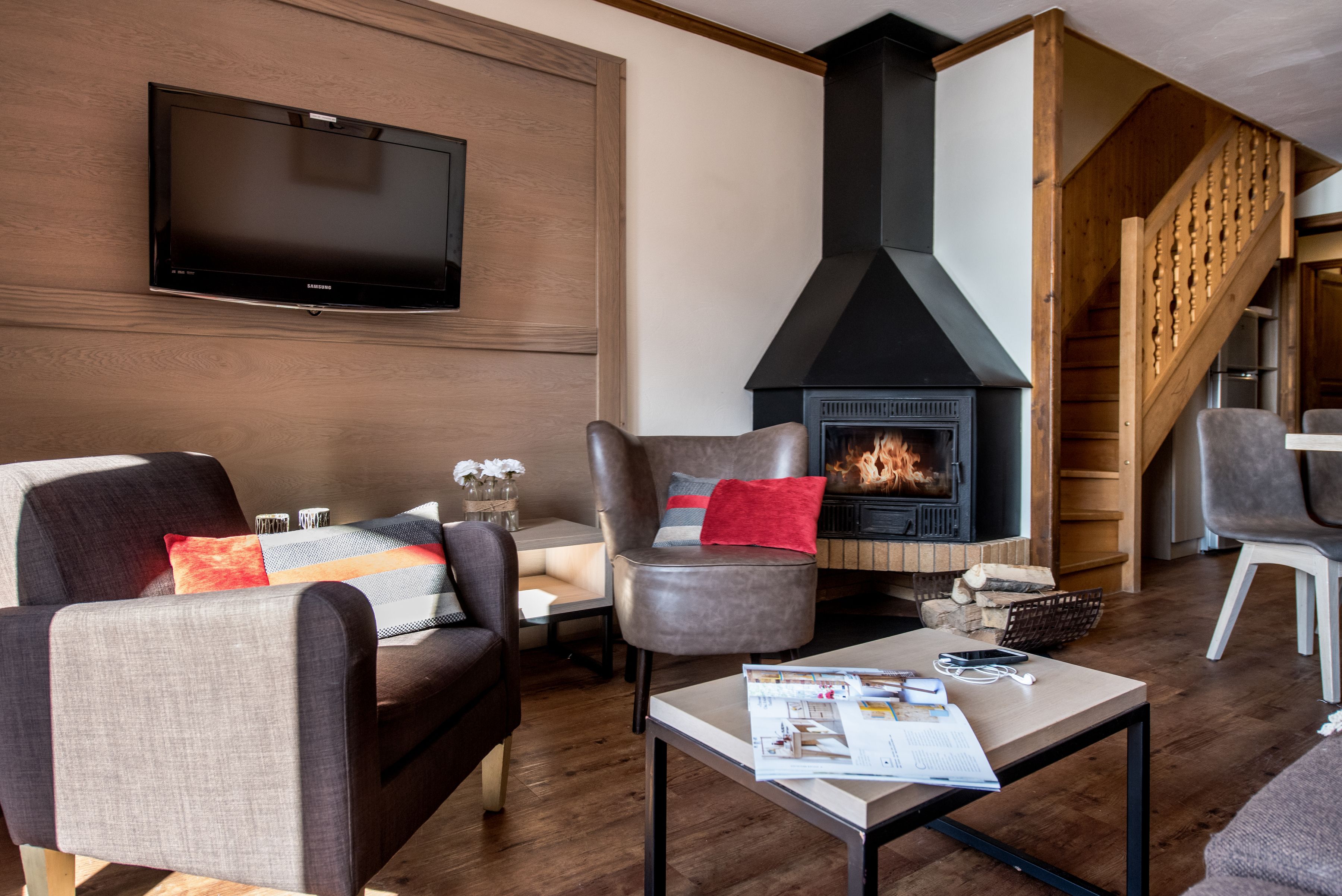 A living room with a fireplace, a flat-screen TV mounted on the wall, and a staircase leading to an upper level.