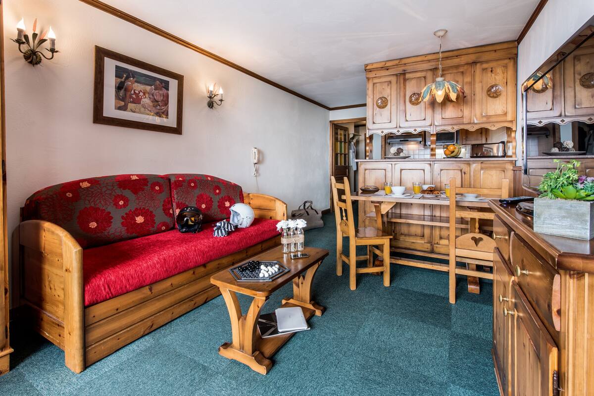 Un salon chaleureux avec un canapé en bois, une petite table en bois et un coin repas comprenant des chaises et des meubles de rangement en bois.