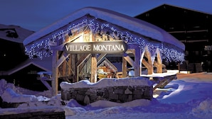A wooden building with a sign reading "VILLAGE MONTANA" and snow-covered surroundings. - Residence Village Montana (Les Belleville)