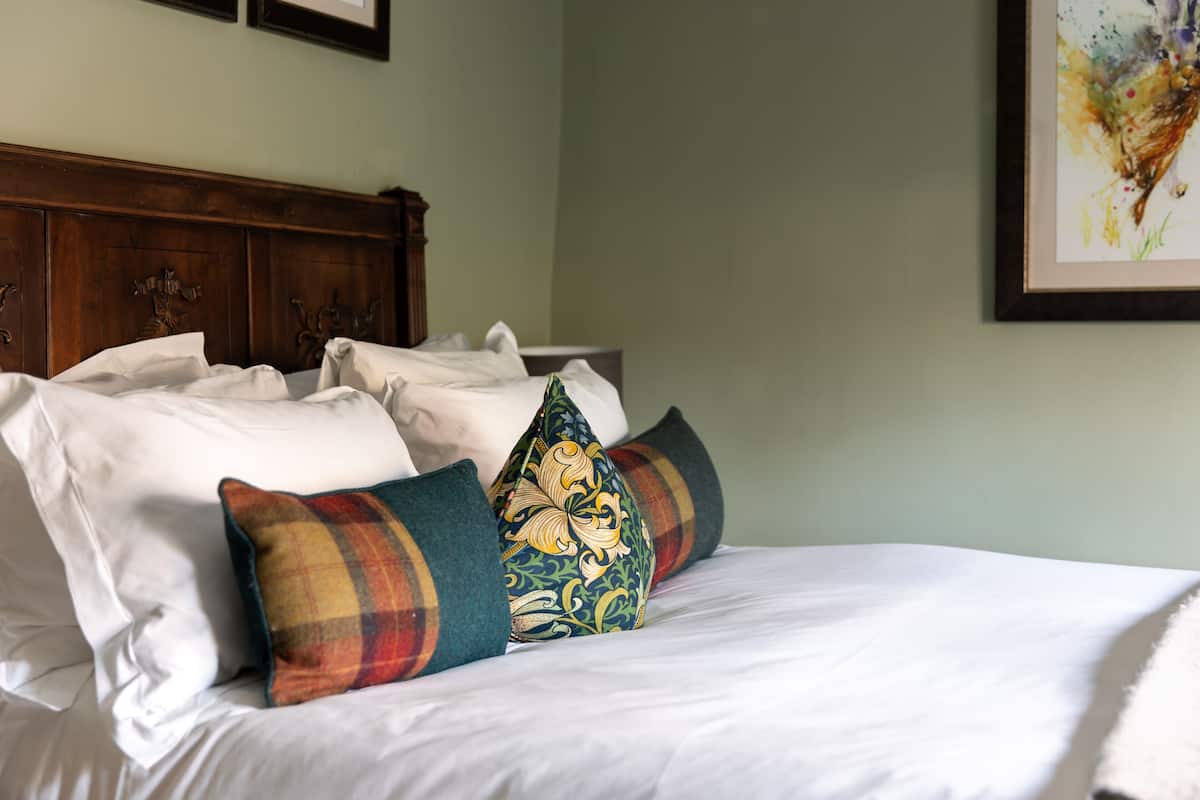 A neatly made bed with white linens and decorative pillows, a wooden headboard, and a framed artwork on the wall.