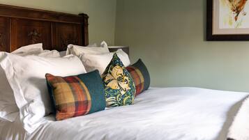 A neatly made bed with white linens and decorative pillows, a wooden headboard, and a framed artwork on the wall.