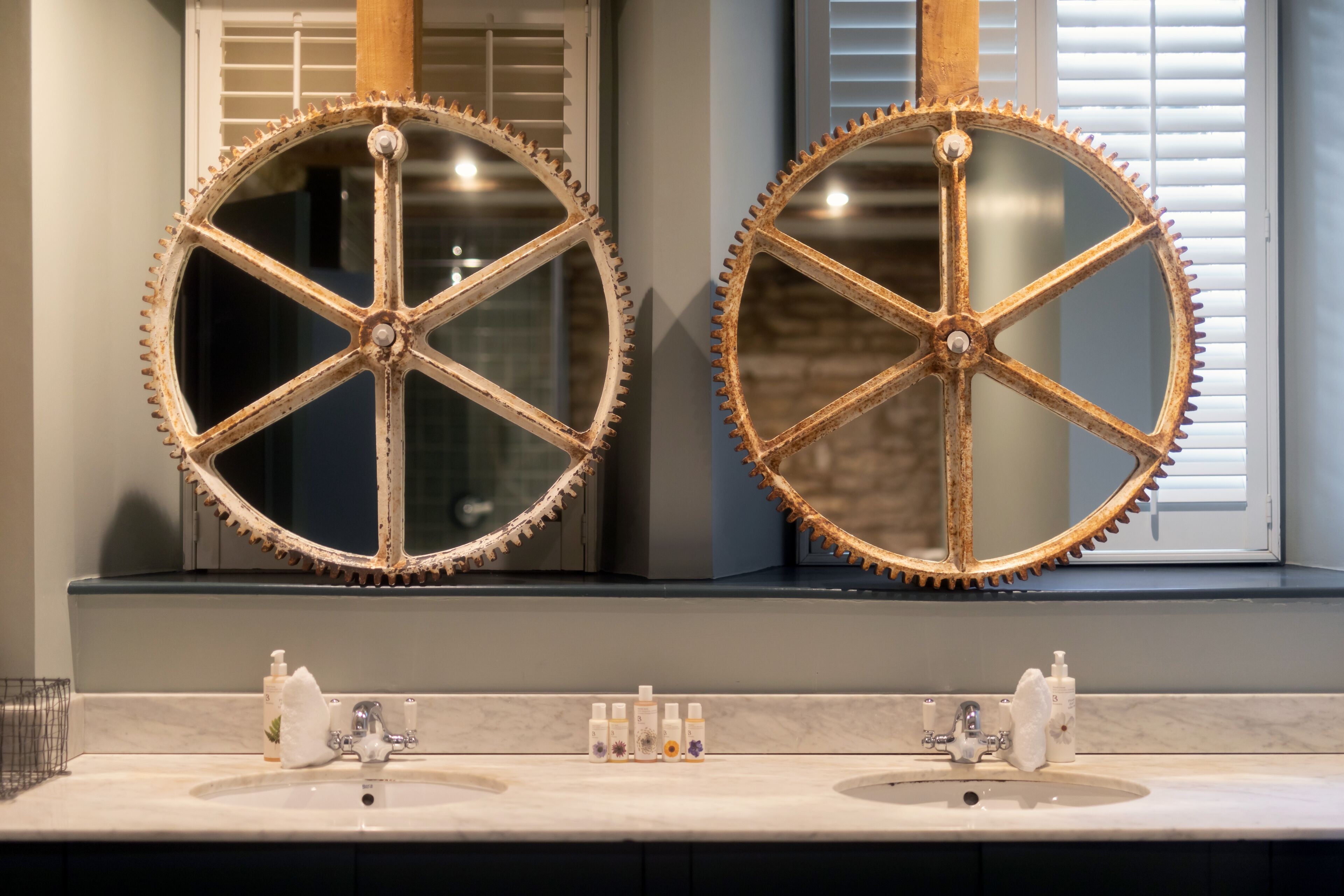 A bathroom with two sinks, a mirror with a gear design, and toiletries on the counter.