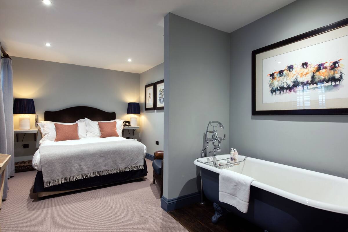 A modern hotel room with a large bed, a classic bathtub, and a framed artwork on the wall.
