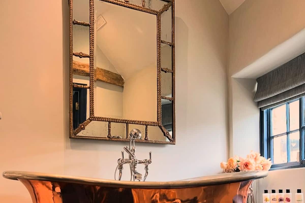 A bathroom with a freestanding copper bathtub, a large mirror, and a window with a view of the outside.