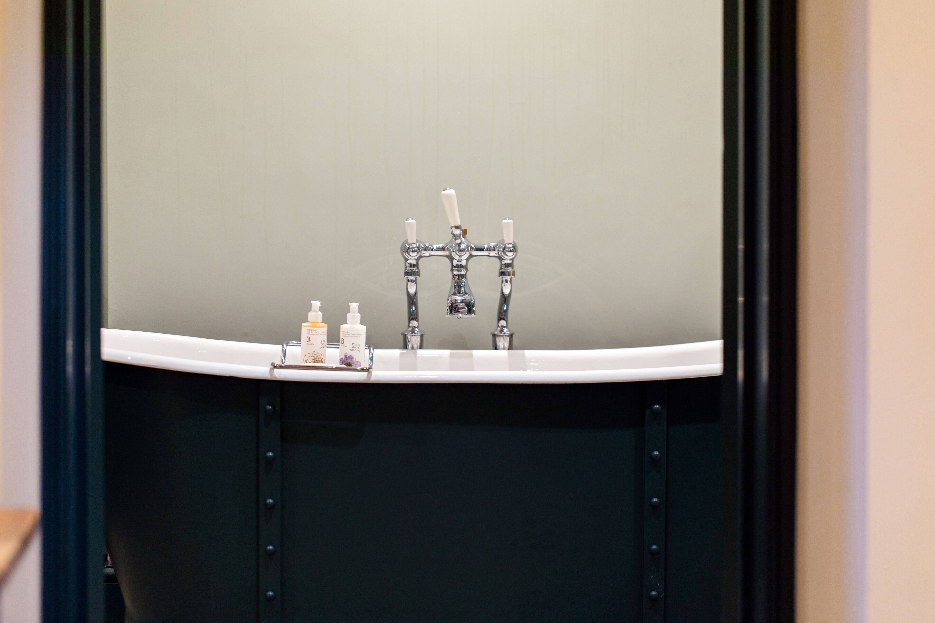 Ein Badezimmer mit einem weißen Waschbecken, zwei Wasserhähnen und drei Kosmetikprodukten auf der Ablagefläche.