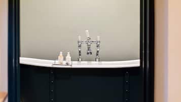 Ein Badezimmer mit einem weißen Waschbecken, zwei Wasserhähnen und drei Kosmetikprodukten auf der Ablagefläche.