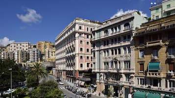 Un hotel histórico con arquitectura clásica, un patio central y vista a la calle con coches aparcados y peatones.