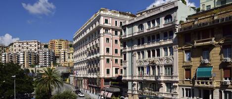 A historic hotel with classic architecture, a central courtyard, and a street view with parked cars and pedestrians.