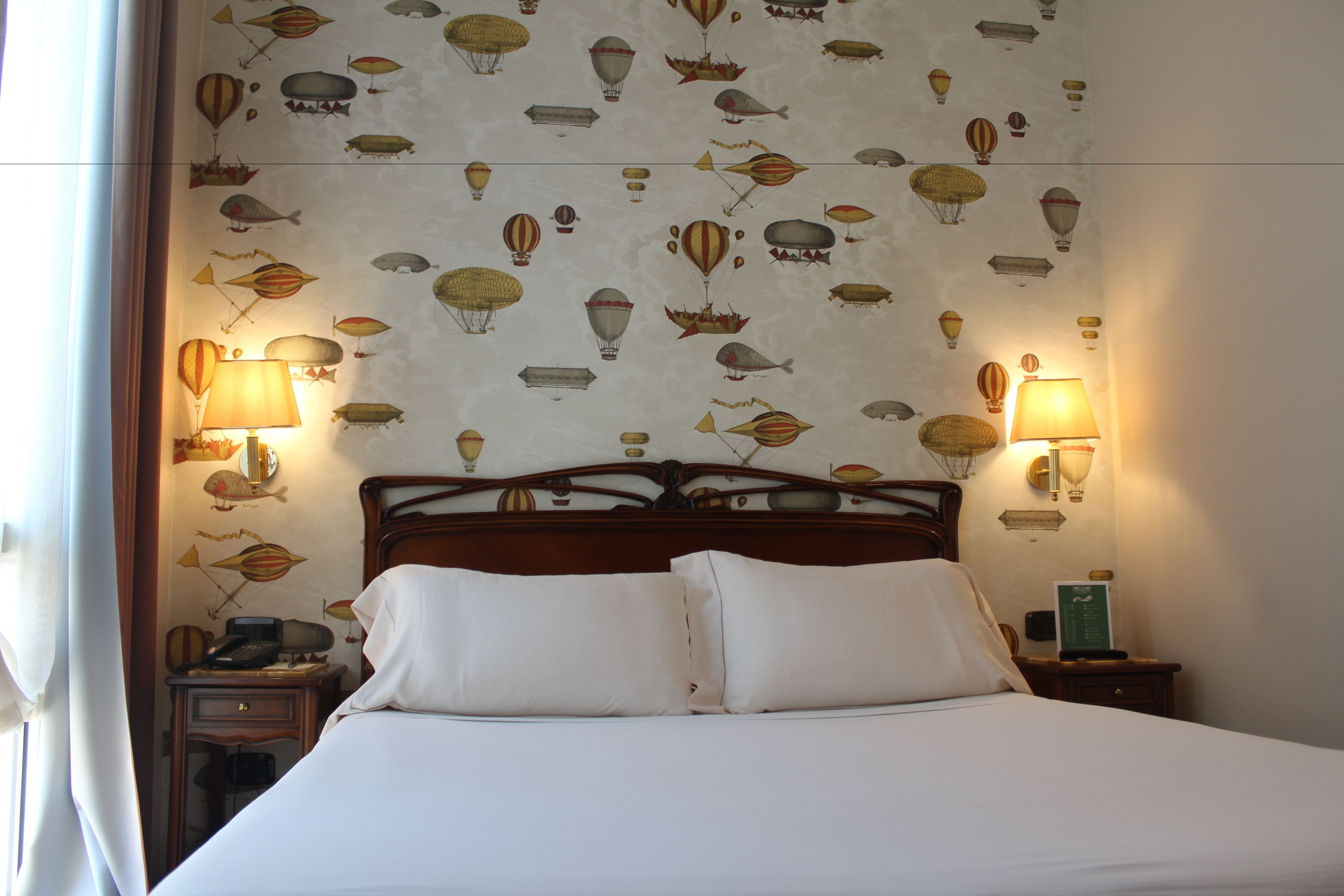 A hotel room with a bed, two bedside tables, and a wall with a pattern of hot air balloons.