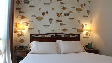 Una habitación de hotel con una cama, dos mesitas de noche y una pared decorada con un dibujo de globos aerostáticos.