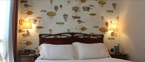 Una habitación de hotel con una cama, dos mesitas de noche y una pared decorada con un dibujo de globos aerostáticos.