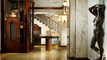 A grand lobby with a marble staircase, a wooden reception desk, and a statue.