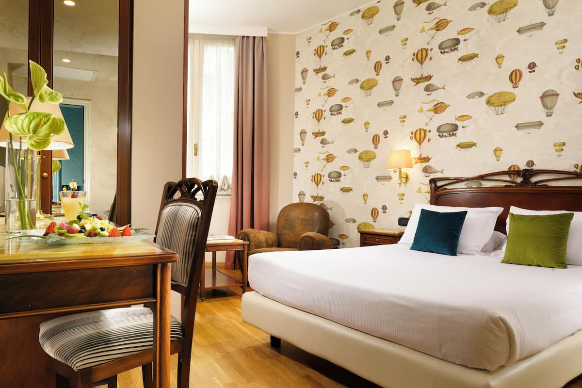 Una habitación de hotel con una cama grande, un escritorio de madera, una silla y un espejo.