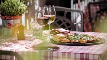 Ein Tisch mit karierter Tischdecke, einem Glas Rotwein, einem Glas Weißwein, einem kleinen Topfpflanzen und einer Pizza.