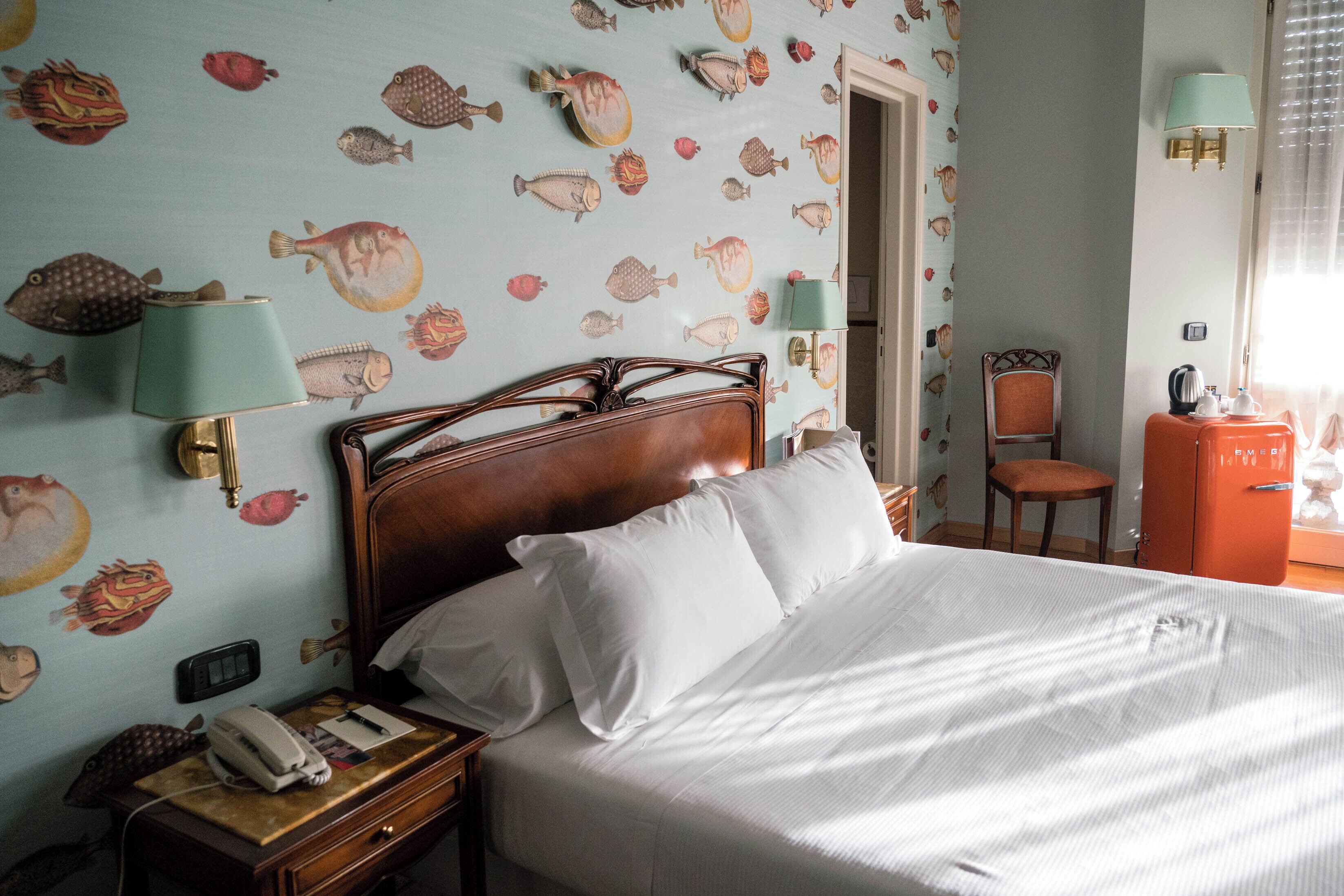 Una habitación de hotel con cama, mesita de noche, teléfono, lámpara y una silla.