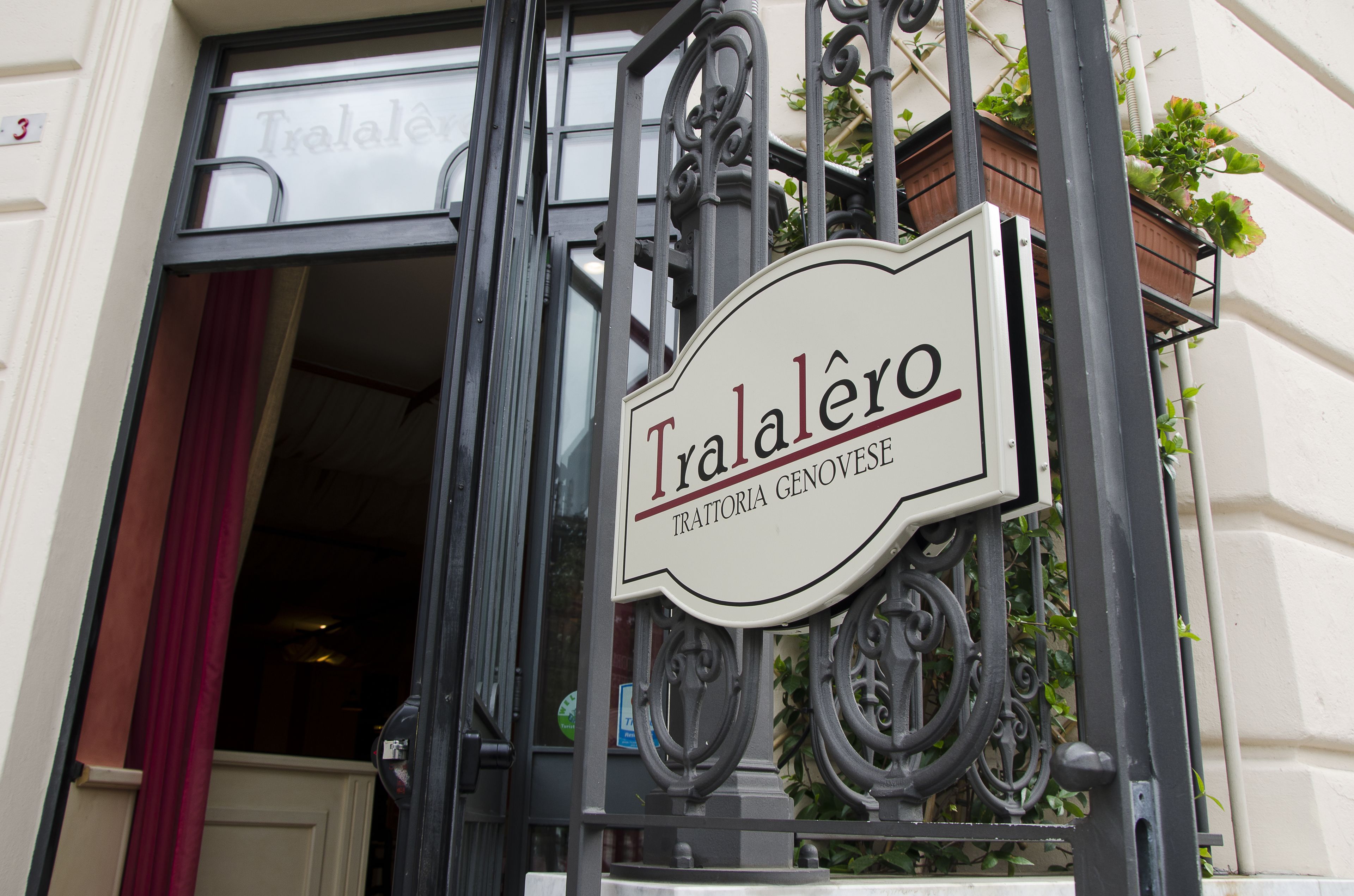 Schild für "Tralalero" mit schmiedeeisernem Tor und einem teilweise sichtbaren roten Vorhang.