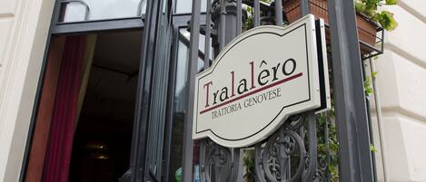 Señal de 'Tralalero' con una reja de hierro forjado y una cortina roja visiblemente a medio cerrar.