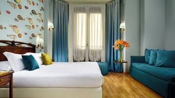Een hotelkamer met een groot bed, een blauwe sofa, een houten nachtkastje en een muur met behangpapier met een vispatroon.