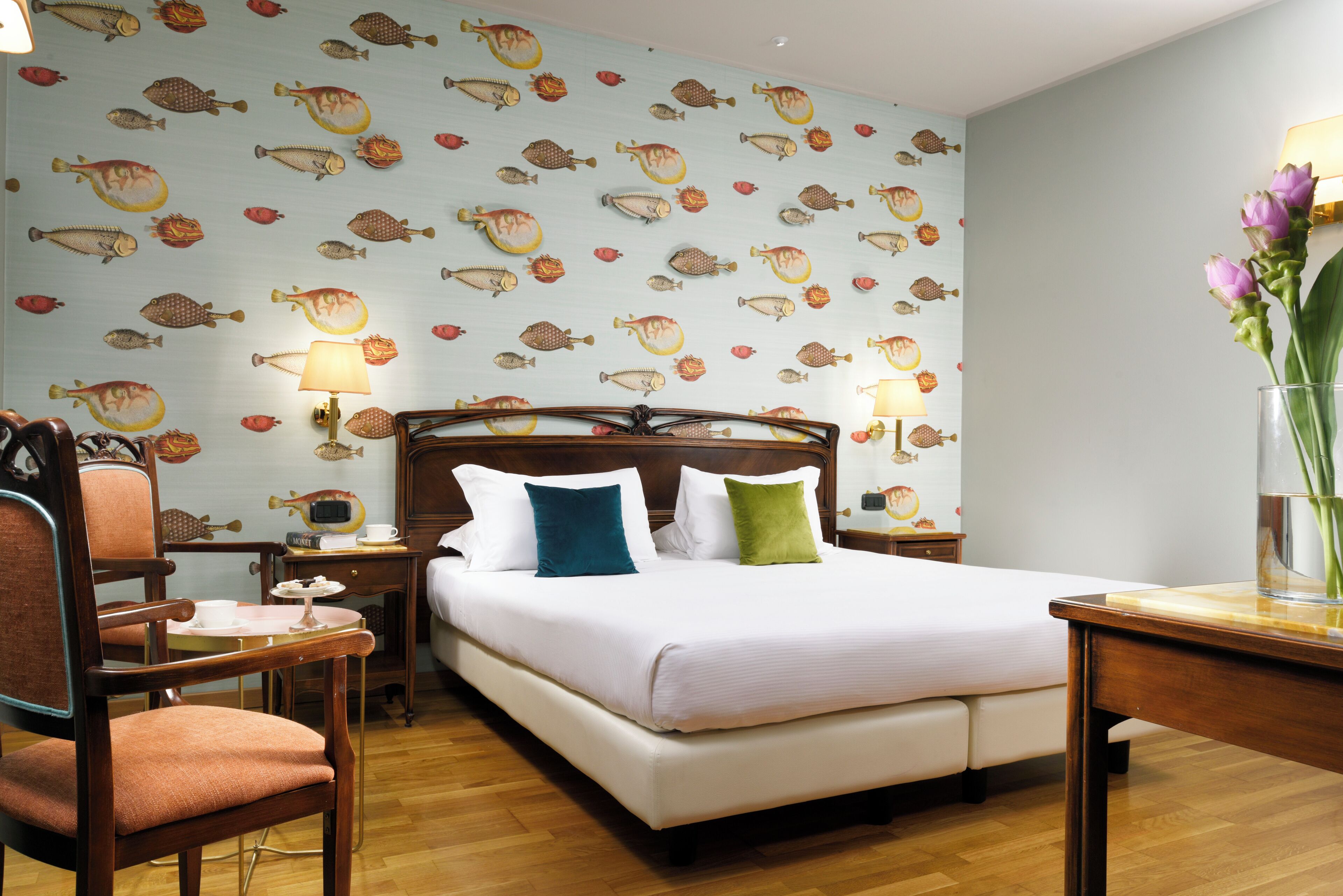 Una habitación de hotel ordenada con cama, sill ón, mesita de noche y lámpara.