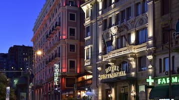Un hotel con un letrero llamativo, balcones y una farmacia al otro lado de la calle.