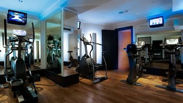 Ein Fitnessstudio mit unterschiedlicher Trainingsausstattung, darunter Laufbänder und Crosstrainer, sowie ein großer Spiegel, der den Raum widerspiegelt.