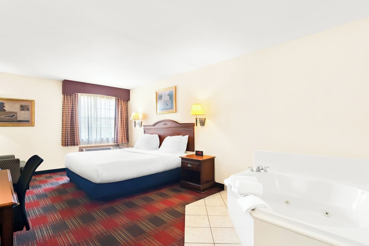 Een hotelkamer met een bed, een bureau, een stoel, een nachtkastje met een lamp en een bad.