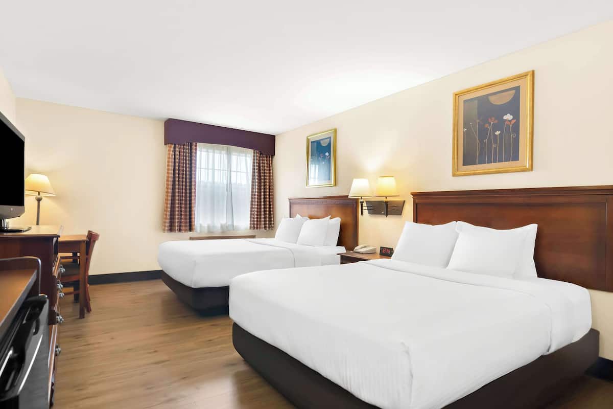 Een hotelkamer met twee bedden, een bureau, een televisie en een raam met gordijnen.
