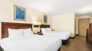 Habitación de hotel con dos camas, cabecera de madera, mesita de noche con lámpara y dos cuadros en la pared.