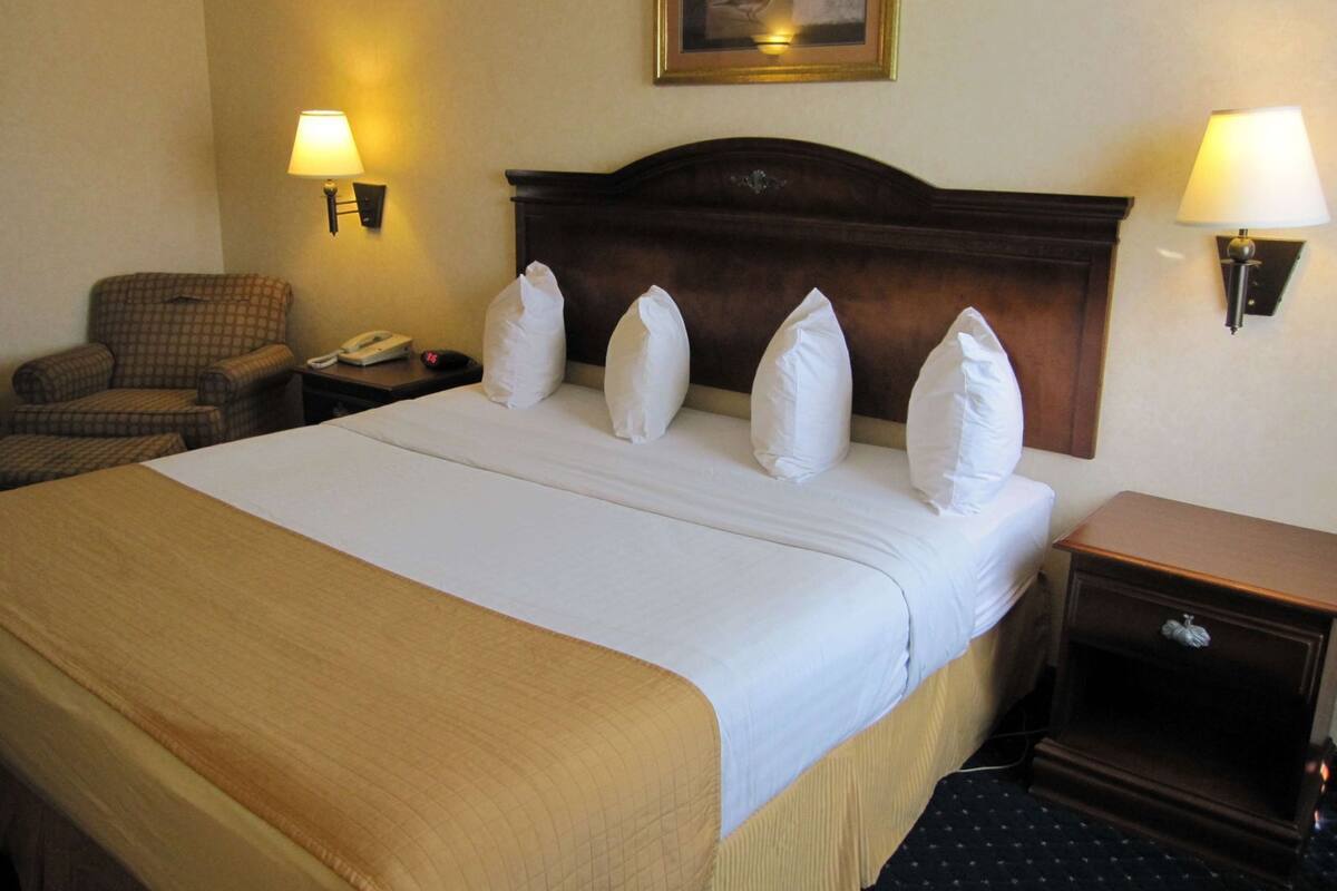 Een hotelkamer met een bed, een stoel, een nachtkastje, een lamp en een schilderij aan de muur.