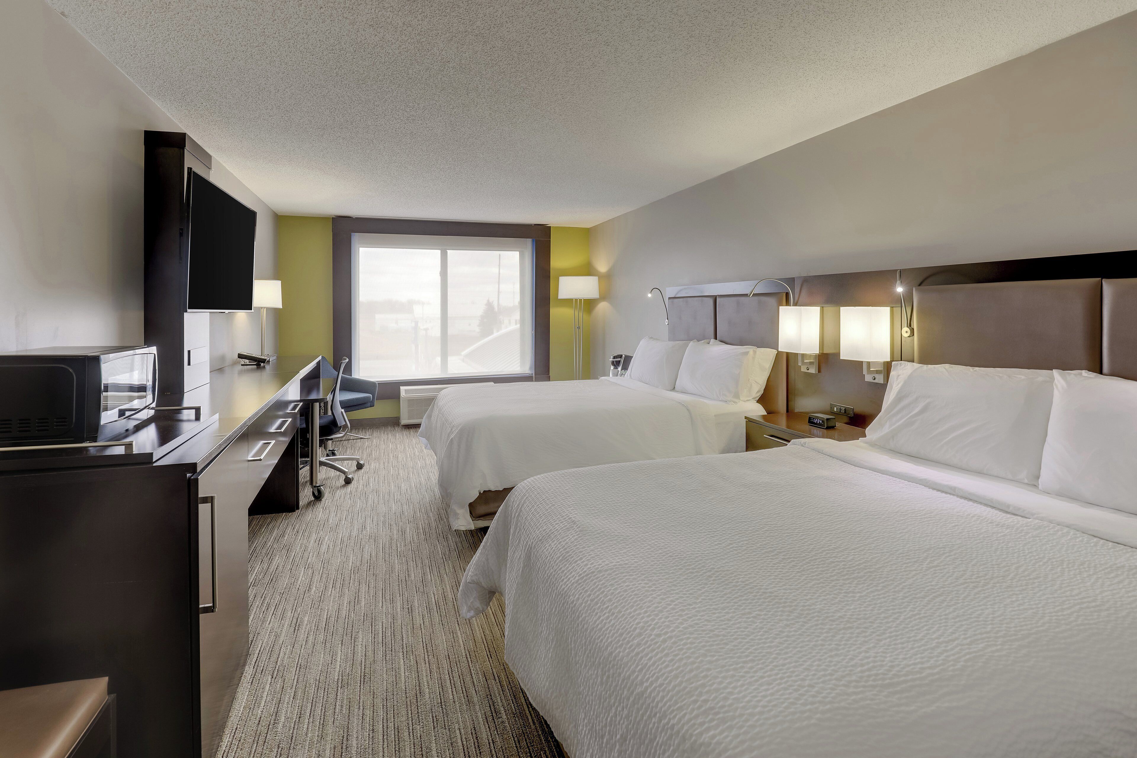 Quarto de hotel com duas camas, uma escrivaninha com computador, televisão e janela com vista.