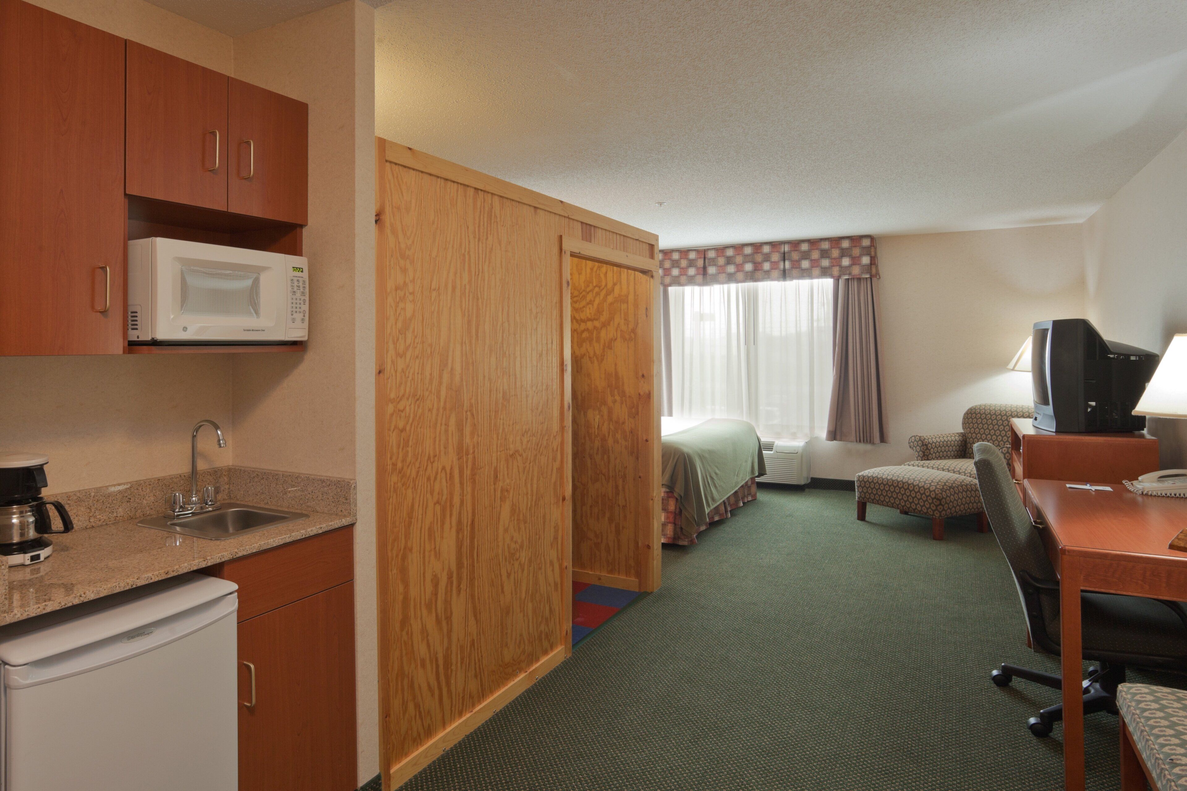 Habitación de hotel con kitchenette, cama, escritorio con silla y televisor.