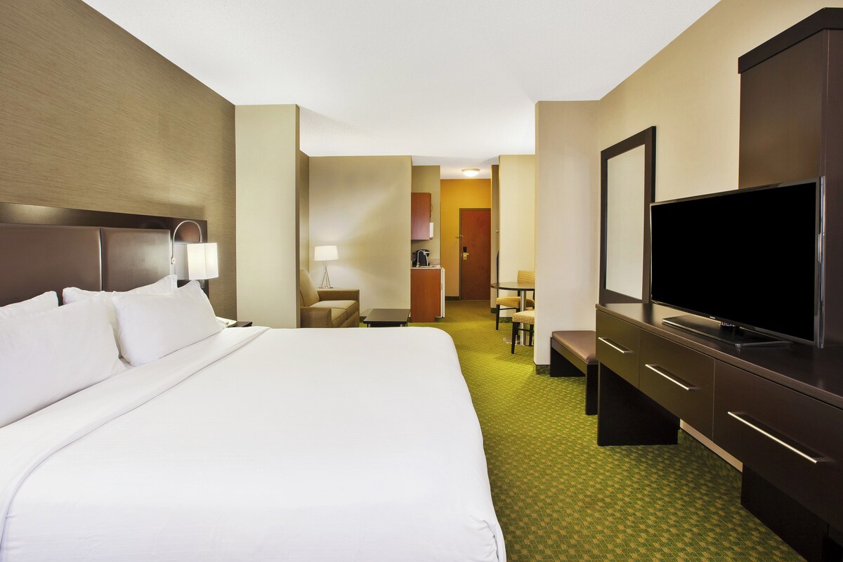 A hotel room with a large bed, a desk, a television, and a bathroom visible through an open door.