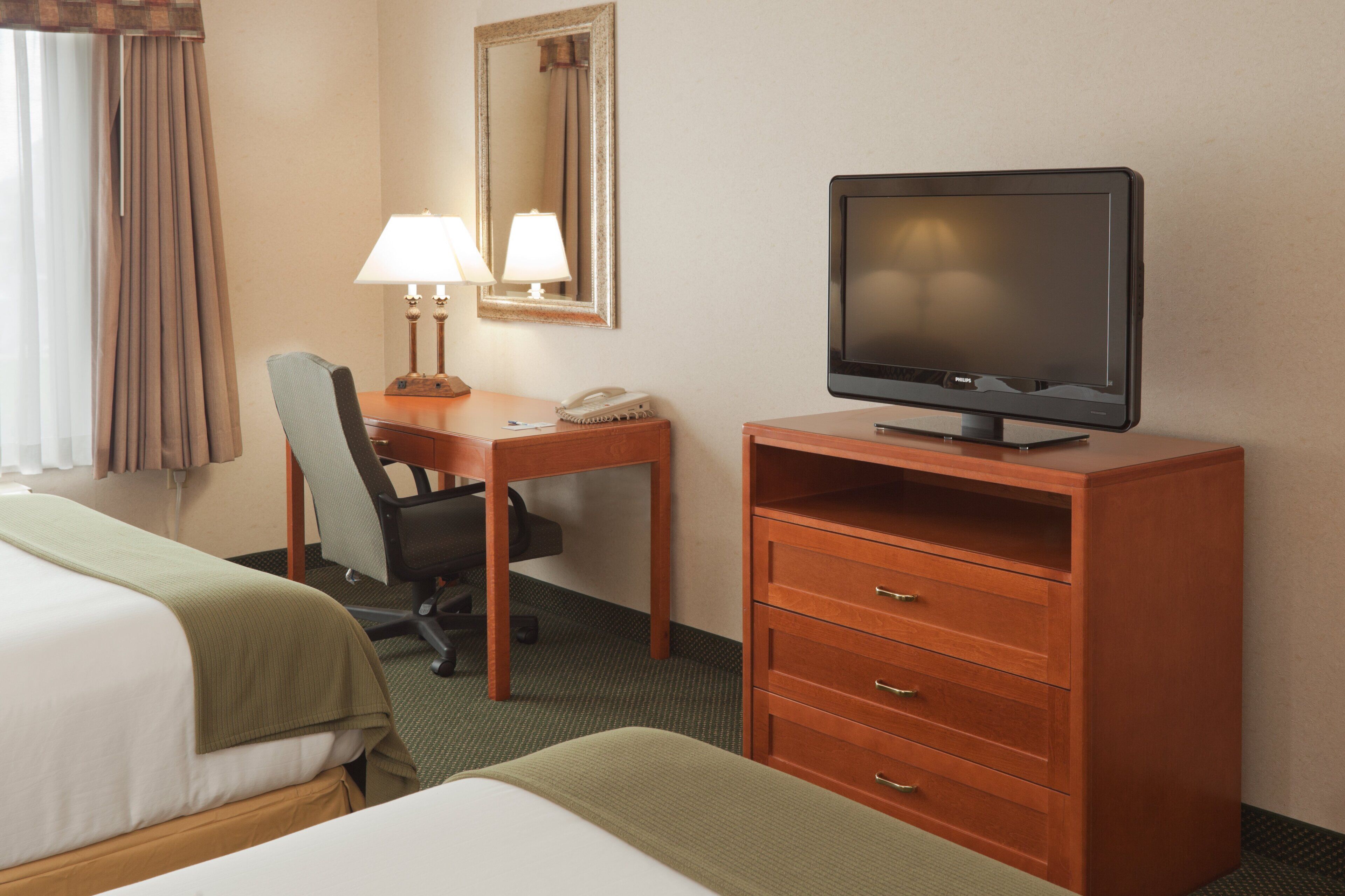 Habitación de hotel con cama, escritorio, silla, televisor, teléfono y espejo.