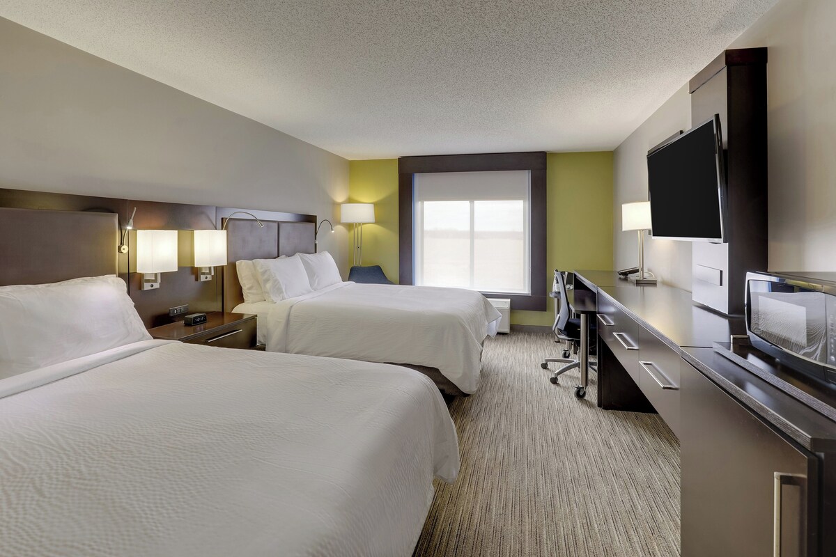Quarto de hotel com duas camas, uma escrivaninha, televisão e janela.