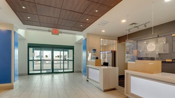 A hotel reception area with a modern design, featuring a reception desk, glass doors leading to the lobby, and a ceiling with recessed lighting. - Holiday Inn Express & Suites Montpelier by IHG (Montpelier)
