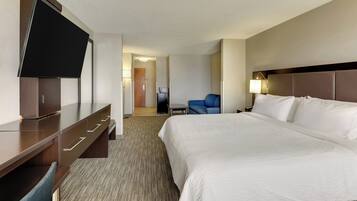 A hotel room with a large bed, a flat-screen TV, a desk with drawers, a chair, and a small table.