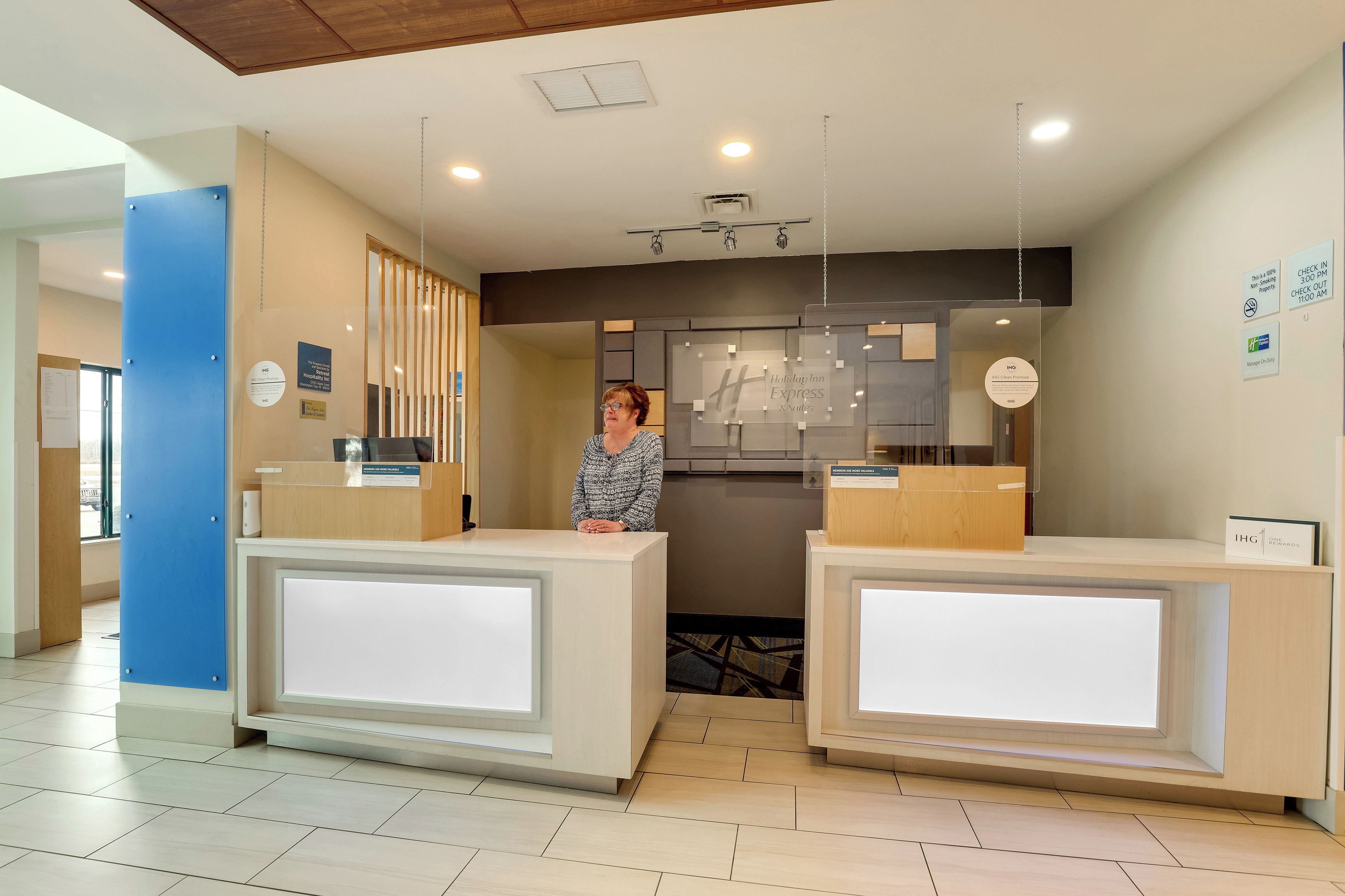 A reception desk with a woman standing behind it, a blue pillar, and a sign indicating a 100% non-smoking property.