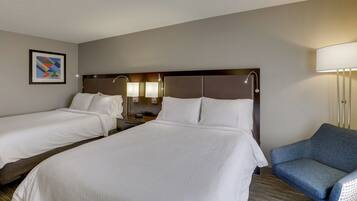 A hotel room with two beds, a nightstand, a lamp, and a blue armchair.