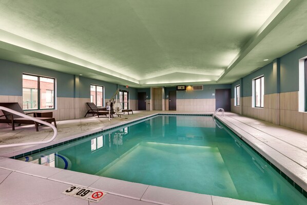 An indoor swimming pool with clear water, a diving board, and lounge chairs.