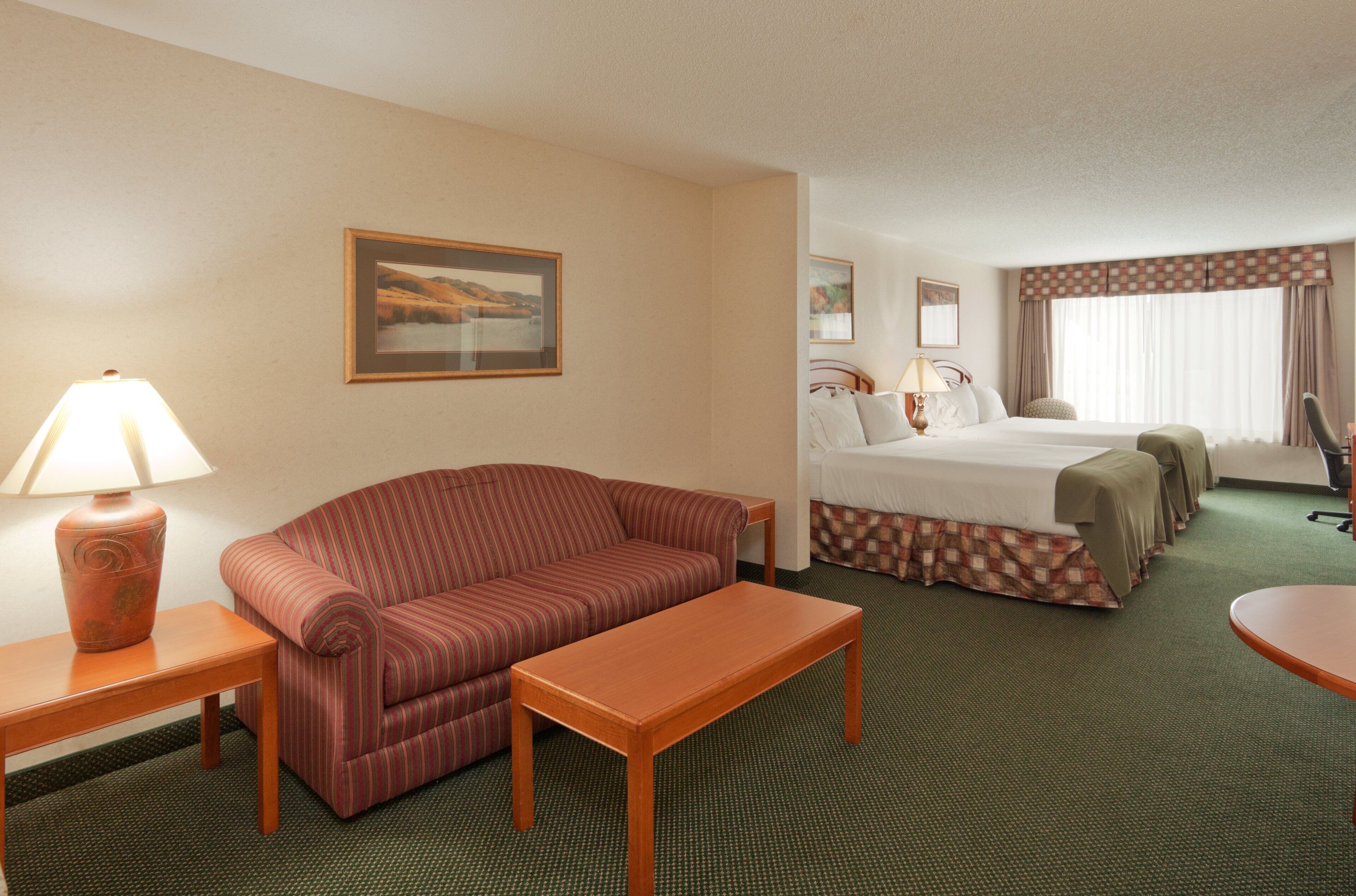 A hotel room with a bed, a sofa, a table, and a lamp.