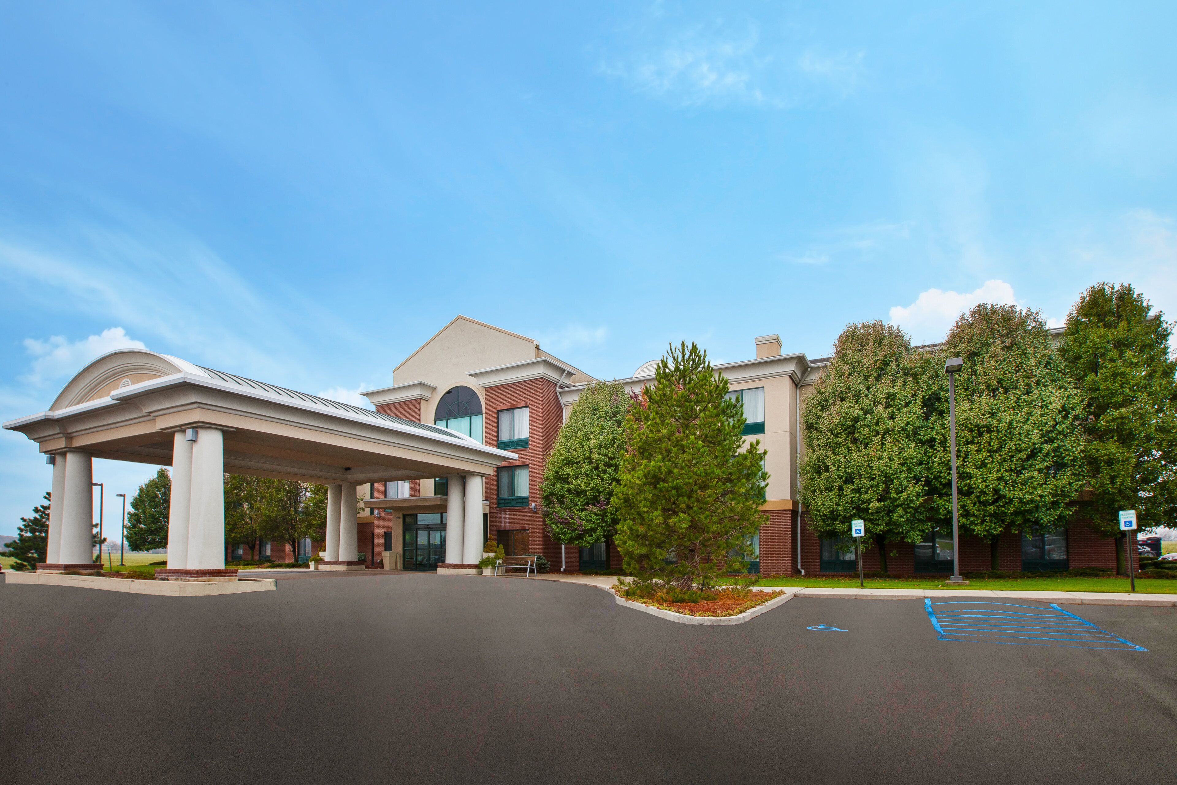 A hotel with a covered entrance, a parking lot, and trees.
